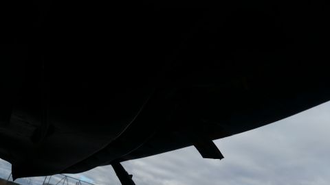 1991 Ford LTD Crown Victoria - Underside view of a black vehicle, showing part of the chassis and a small flap against a cloudy sky.