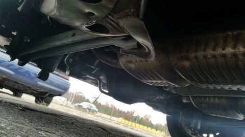 1991 Ford LTD Crown Victoria - A low-angle shot reveals the undercarriage of a vehicle, showing its exhaust system and suspension parts, with another vehicle visible in t…