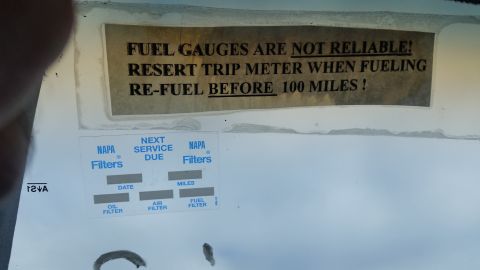 1991 Ford LTD Crown Victoria - Photograph of a fuel-gauge warning sticker and a NAPA service-due maintenance label affixed to a vehicle, not a classifiable technical docu…