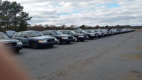 1991 Ford LTD Crown Victoria - Multiple Ford Crown Victoria Police Interceptors are lined up in an outdoor lot under a cloudy sky.