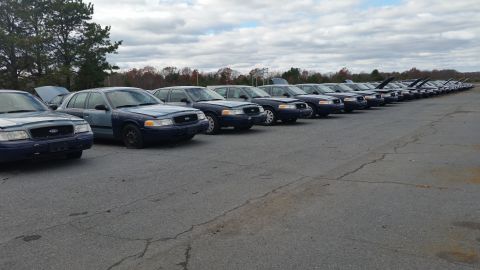 1991 Ford LTD Crown Victoria - A long line of Ford Crown Victoria Police Interceptors are parked in an outdoor lot under a cloudy sky.