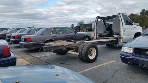 1991 Ford LTD Crown Victoria - A cutaway chassis of a white van is parked in a lot with several Ford Crown Victoria sedans, suggesting a fleet vehicle auction or disposal.