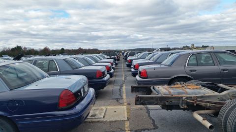 1991 Ford LTD Crown Victoria - Multiple Ford Crown Victoria Police Interceptor sedans are parked in rows under a cloudy sky.