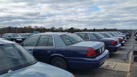 1991 Ford LTD Crown Victoria - Several Ford Crown Victorias are parked in a lot under a cloudy sky. The closest car has writing on its window.