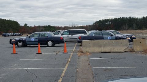 1991 Ford LTD Crown Victoria - Several police vehicles are parked in an outdoor lot under an overcast sky.
