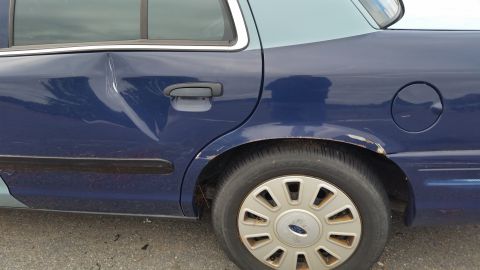 1991 Ford LTD Crown Victoria - The rear passenger side door of a blue Ford Crown Victoria shows significant damage and rust near the wheel arch.
