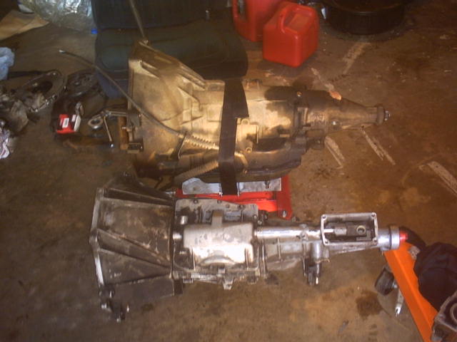 Two dirty automatic transmissions are on the floor, one on a red stand