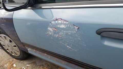1991 Ford LTD Crown Victoria - The side of a blue vehicle shows extensive damage to the paintwork, revealing rust underneath.