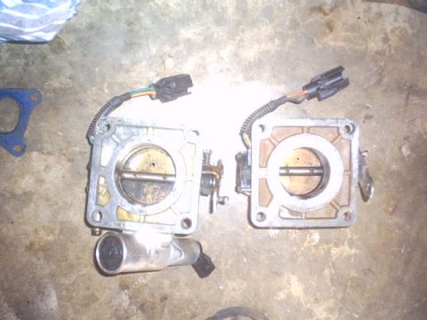 1991 Ford LTD Crown Victoria - Two throttle bodies with electrical connectors are shown on a concrete surface.
