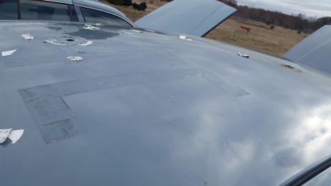 1991 Ford LTD Crown Victoria - The hood of a gray car shows numerous patches of tape and several holes.
