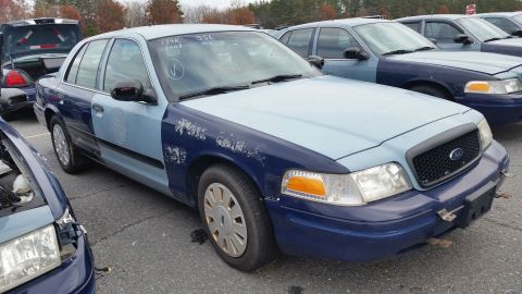 1991 Ford LTD Crown Victoria - A two-tone blue sedan with visible body damage and mismatched panels sits in a lot with other vehicles.