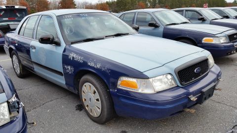 1991 Ford LTD Crown Victoria - A two-tone police car, likely a Ford Crown Victoria, is parked in a lot with other similar vehicles. The car shows significant wear and tea…