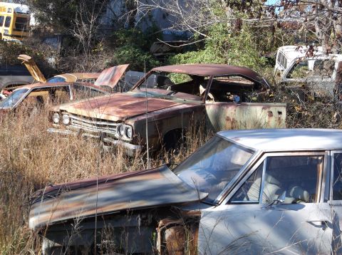 1974 Dodge Challenger - A heavily rusted 1969 Plymouth Road Runner sits in a junkyard, partially obscured by other vehicles and tall grass.