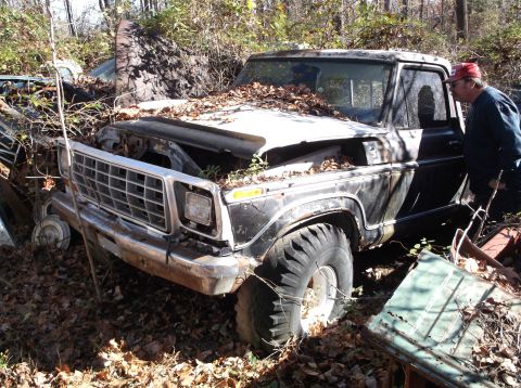 1974 Dodge Challenger - A man inspects a weathered pickup truck sitting amongst debris and other vehicles in an outdoor junkyard.