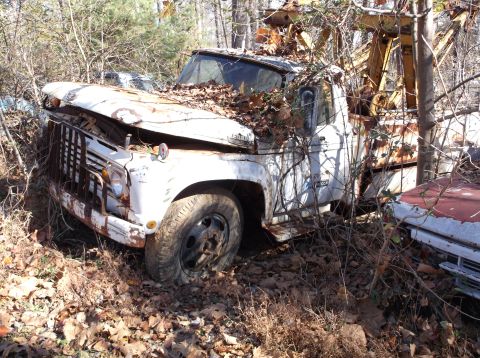 1974 Dodge Challenger - An old tow truck sits abandoned in a wooded area, overgrown with vegetation and leaves.