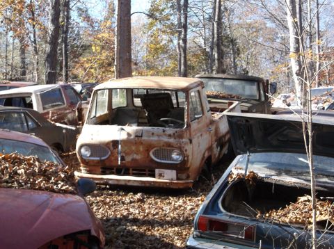 1974 Dodge Challenger - A weathered van sits among other vehicles in a junkyard, its front grille and headlights visible.