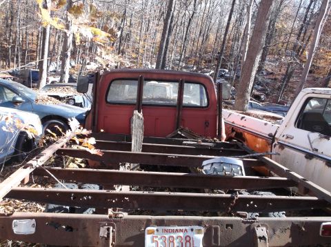 1974 Dodge Challenger - A red pickup truck cab sits in a junkyard, surrounded by other vehicles and trees.