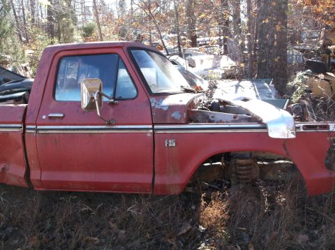 1974 Dodge Challenger - A weathered red 1975 Ford F-150 pickup truck sits in a junkyard with its hood open.