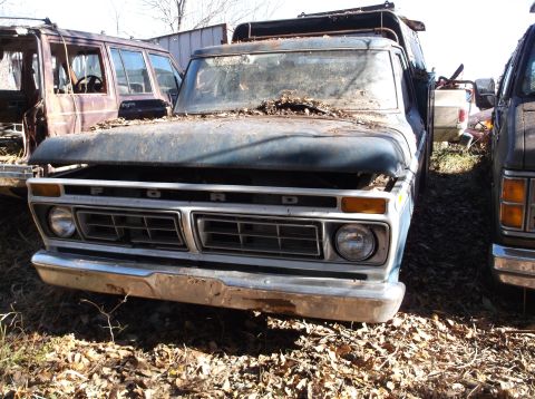 1974 Dodge Challenger - A weathered Ford truck sits in a junkyard, its grille clearly visible.