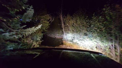 1996 Ford Bronco - Headlights cut through the darkness on a wooded trail, illuminating the path ahead.