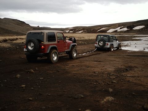 1996 Ford Bronco - Two Jeep Wranglers navigate a challenging, muddy landscape, with one vehicle assisting the other.
