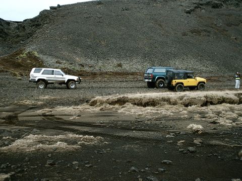 1996 Ford Bronco - Three SUVs traverse a , off-road terrain under a cloudy sky.