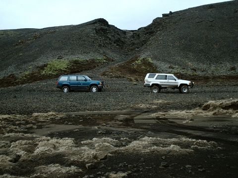 1996 Ford Bronco - Two SUVs are parked on a rocky, barren landscape under an overcast sky.