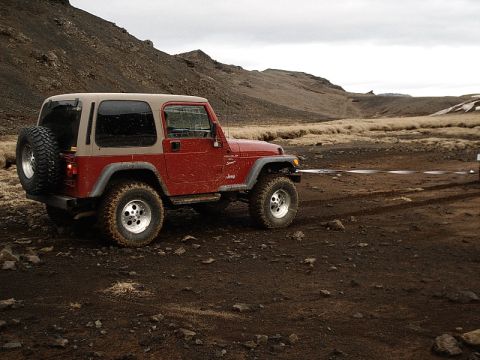 1996 Ford Bronco - A red Jeep Wrangler is parked on a dirt road in a barren, mountainous landscape under a cloudy sky.