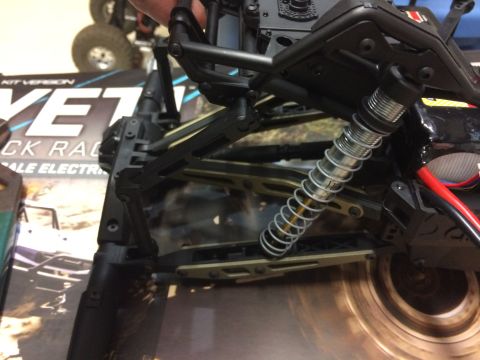 1989 Ford Bronco - Close-up of an RC car's suspension system, with a partial view of another vehicle in the background.