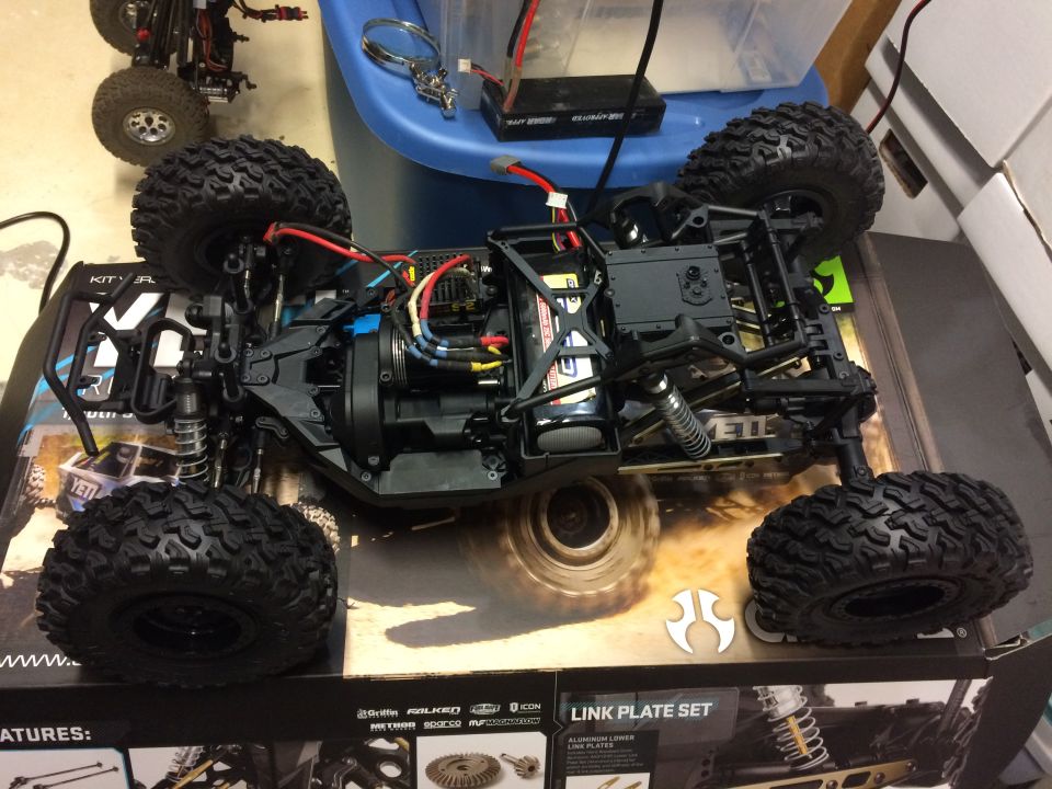 RC car chassis with large tires and visible electronics, another RC car in background