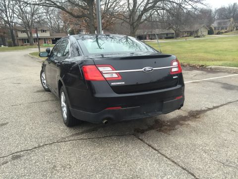 2013 Ford Taurus - This black Ford sedan is parked in a lot with houses and trees in the background.