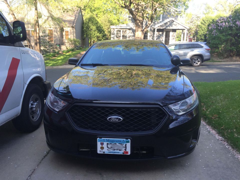 Black 2013 Ford Taurus police car front view, parked next to a white van