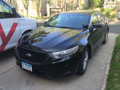2013 Ford Taurus - A black 2013 Ford Taurus sedan is parked on a driveway next to a white van.