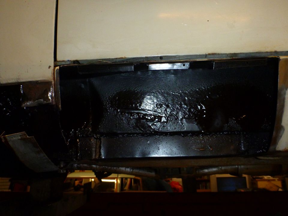 Cream colored vehicle's lower body panel with black undercoating, showing rust and damage