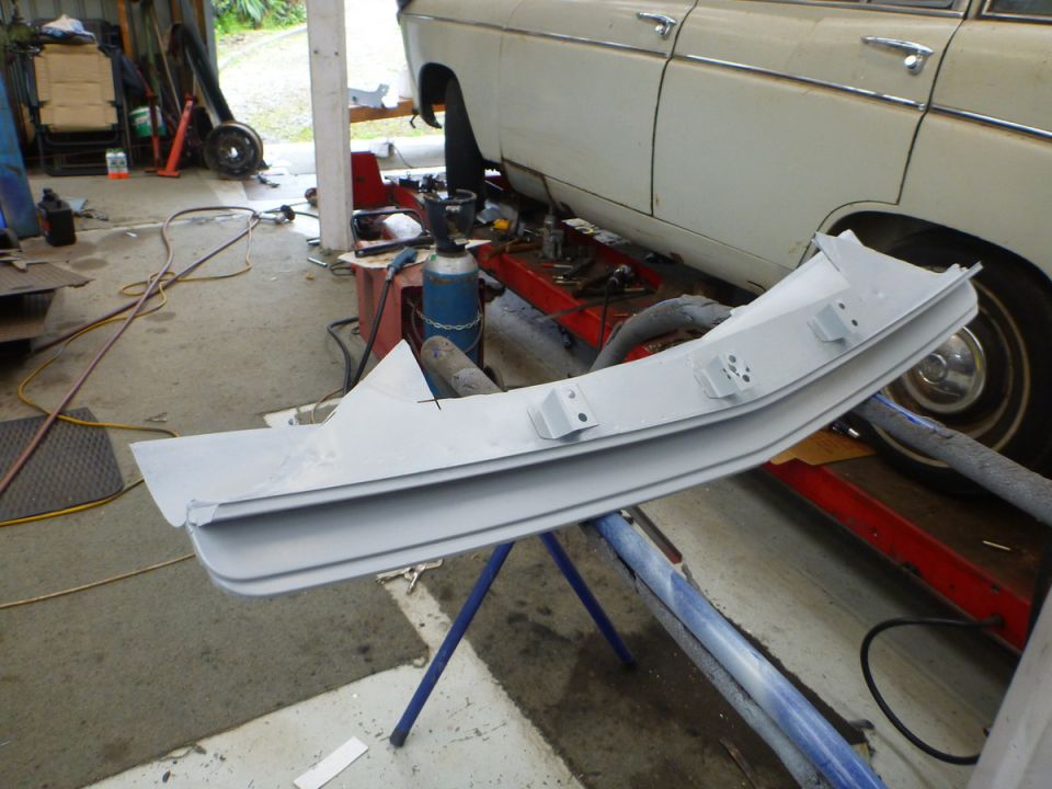 Primer-gray car bumper on stand, white car in background