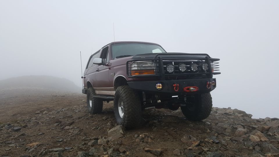 1996 Ford Bronco with aftermarket bumper and lights parked on a rocky hill