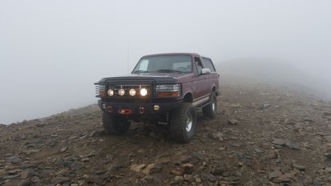 1996 Ford Bronco - A maroon Ford Bronco sits on a rocky mountain path, shrouded in fog.