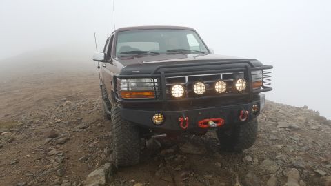 1996 Ford Bronco - A Ford Bronco with a bull bar and auxiliary lights navigates a foggy, rocky mountain path.