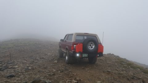 1996 Ford Bronco - A 1996 Ford Bronco navigates a foggy, rocky mountain trail, equipped with auxiliary fuel cans.