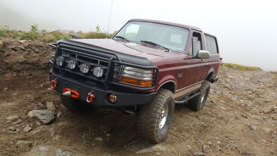 Maroon Ford Bronco with aftermarket bumper and lights on rocky terrain