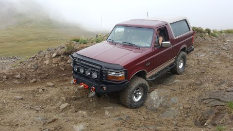 1996 Ford Bronco - A maroon Ford Bronco navigates a rocky, off-road trail under a foggy sky.