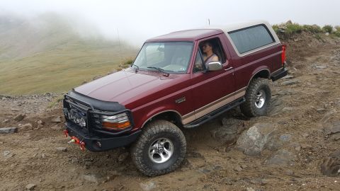 1996 Ford Bronco - A maroon 1992 Ford Bronco navigates a challenging rocky and muddy terrain on a mountain trail.