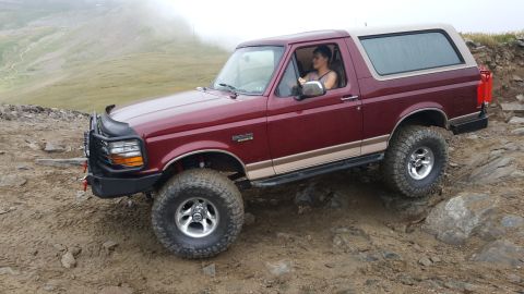1996 Ford Bronco - A red 1996 Ford Bronco with a tan top navigates a rocky mountain path.