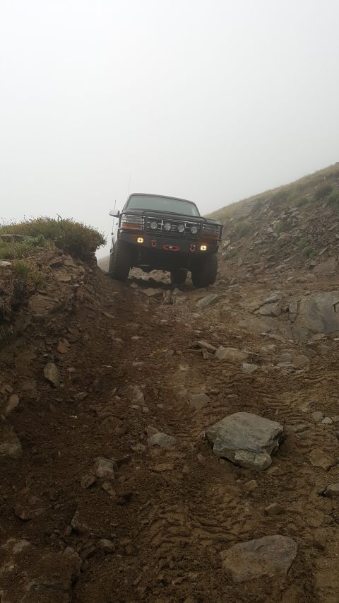1996 Ford Bronco - A black Ford Bronco navigates a steep, rocky, and muddy off-road trail under foggy conditions.