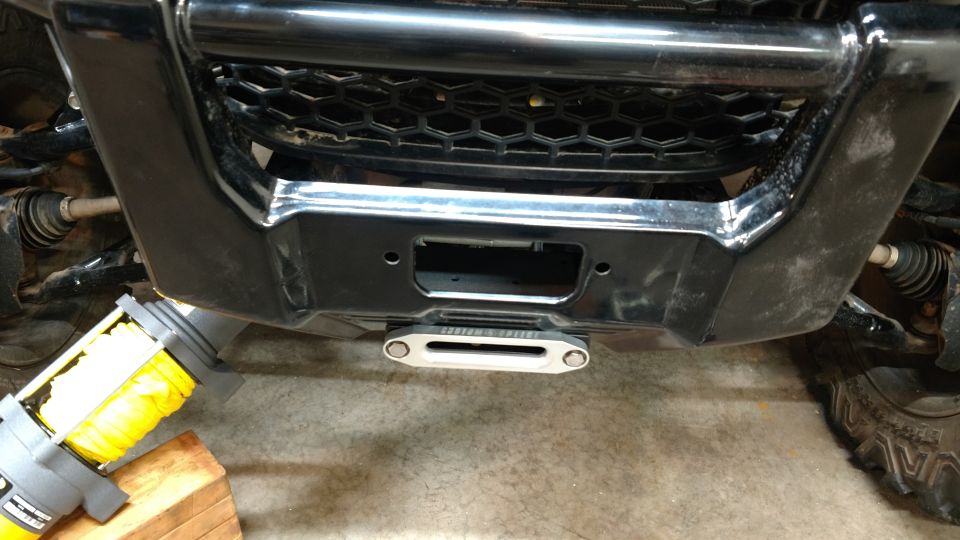 Front bumper of an ATV with a silver winch and yellow rope, showing a black grille and chrome accents