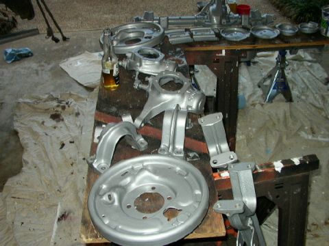 1995 Ford Bronco - Various suspension components and a brake drum, freshly painted silver, are laid out on a workbench with a bottle of beer.
