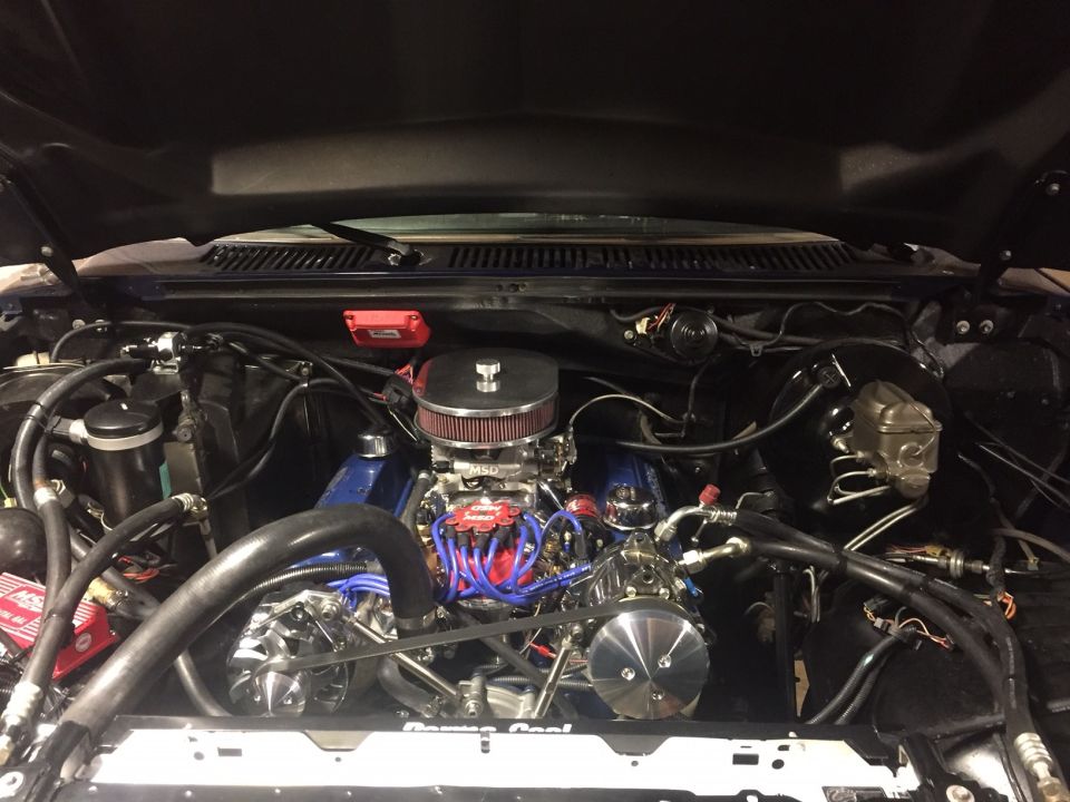 Engine bay with a V8 engine, chrome air cleaner, and blue valve covers. Supermotors.net logo visible