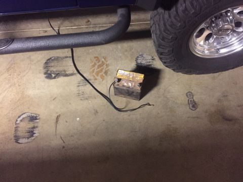 1982 Ford Bronco - An old, rusted car battery sits on a concrete floor near the running board and tire of a vehicle.