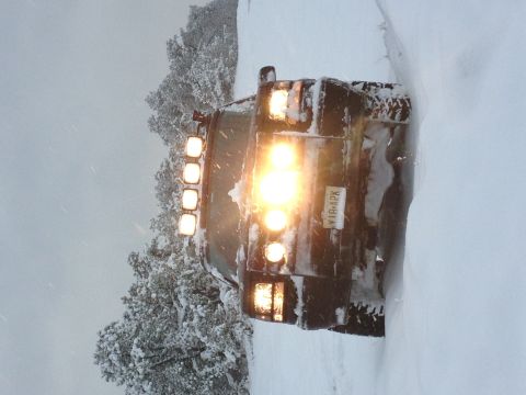 1996 Ford Bronco - An SUV is stuck deep in the snow, its headlights brightly illuminating the winter scene.