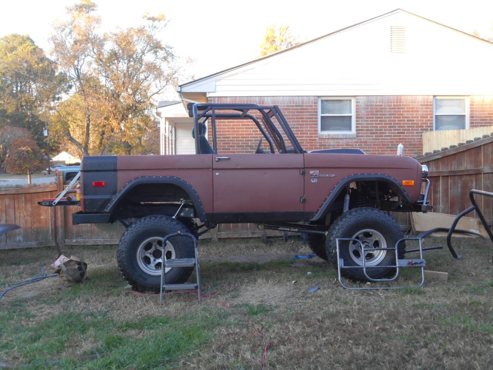 1972 Ford Bronco with roll cage, lifted suspension, and aftermarket wheels, parked in a yard